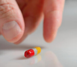 Close up of hand picking up pill: RedLawList Defective Products Blog