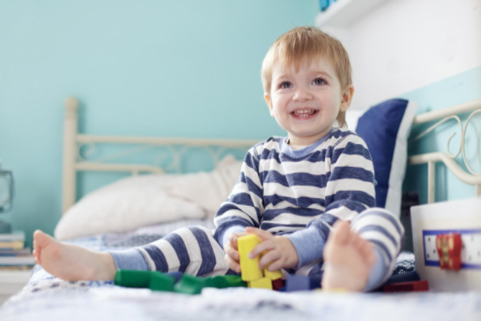 Toddler sitting on bed with toys: RedLawList Accidents and Injuries Blog
